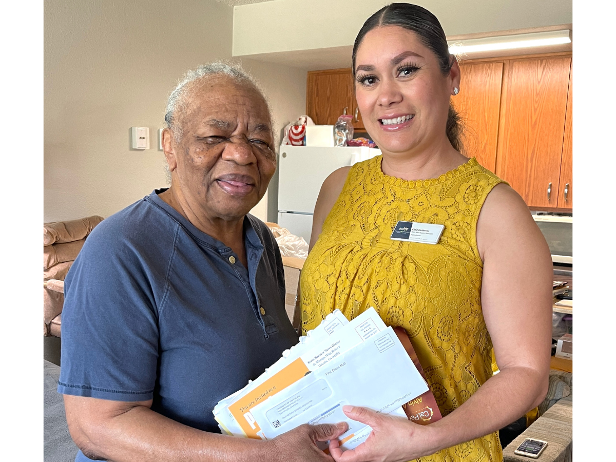 Lidia Gutierrez and Delois M. smiling together while holding mail. 