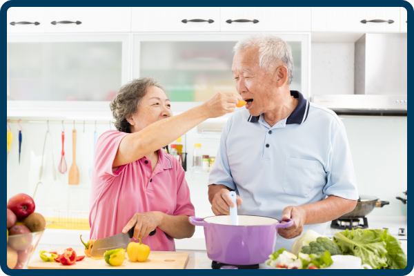 elderly couple feeding each other while cooking 