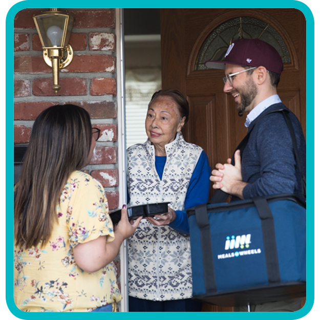 two volunteers handing a senior a tray of food