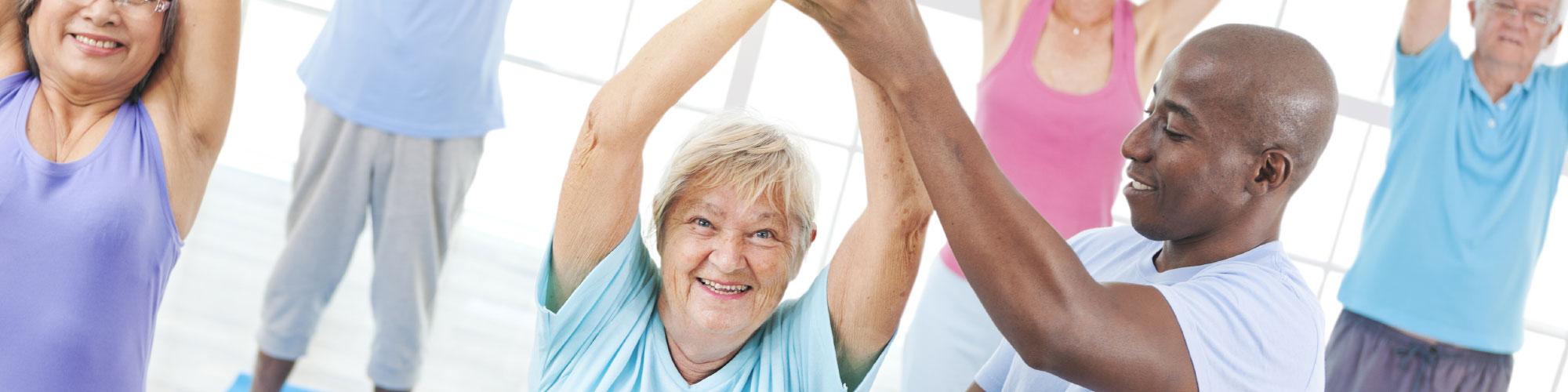 african american exercise coach helping an elderly lady in a class with other seniors