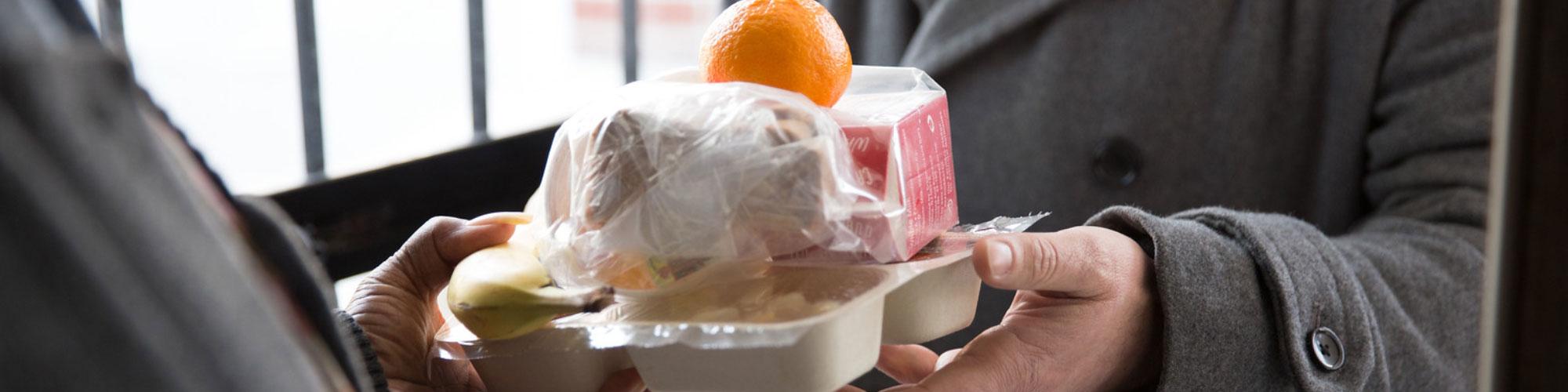 person delivering to a senior a meal with orange and milk and other food