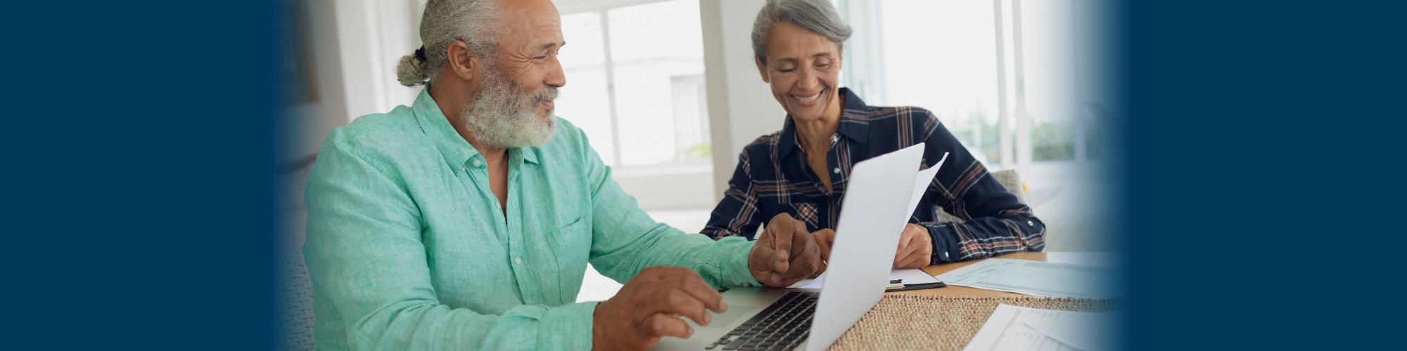 african american couple smiling while looking at a laptop and papers